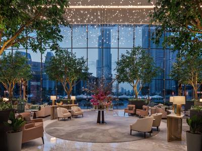 Moderner Lounge-Bereich mit Sitzgruppen, Bäumen und großer Glasfront im Hintergrund bei Abendlicht.