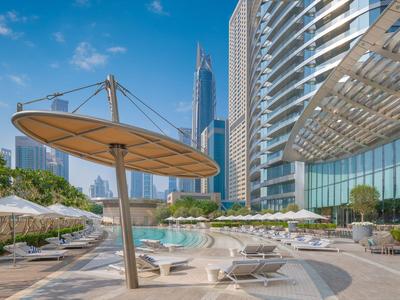 Espace piscine d'hôtel moderne avec parasols et grands immeubles en arrière-plan.