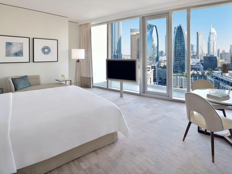 Modernes Hotelzimmer mit großem Bett, Schreibtisch, Stuhl und Panoramafenstern mit Stadtblick.