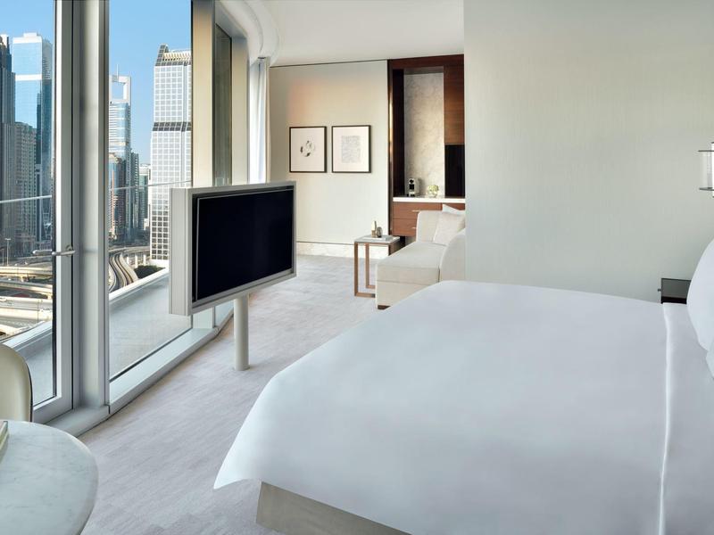 Modernes Hotelzimmer mit großem Bett, freistehendem Fernseher und großem Fenster mit Stadtblick.