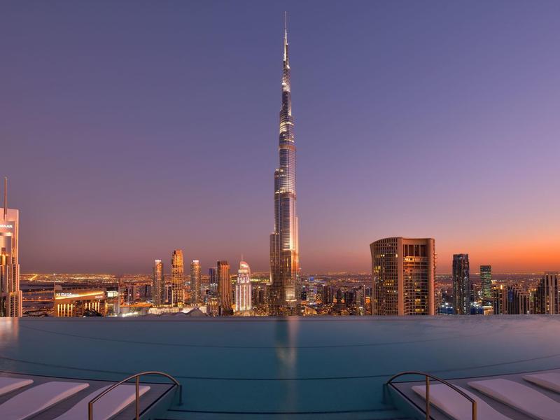 Stadtpanorama bei Sonnenuntergang mit schwimmendem Pool und Burj Khalifa im Hintergrund.