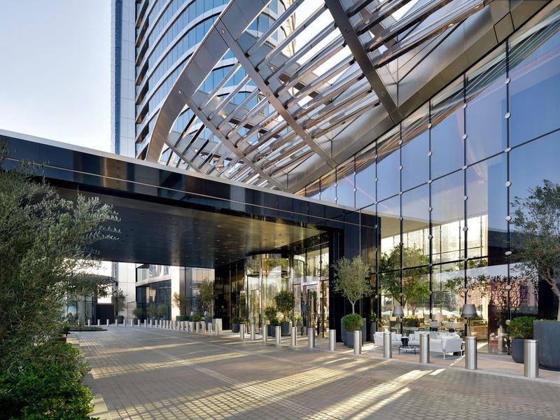 Modernes Hochhaus mit Glasfassade, das von Stahlträgern und Pflanzen umgeben ist.