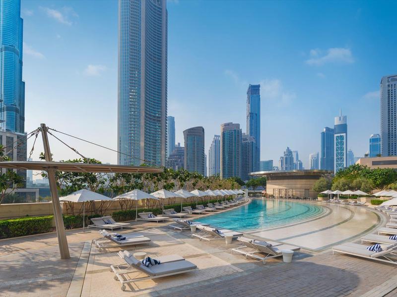 Luxuriöser Außenpool mit Liegen, umgeben von hohen Wolkenkratzern bei blauem Himmel.