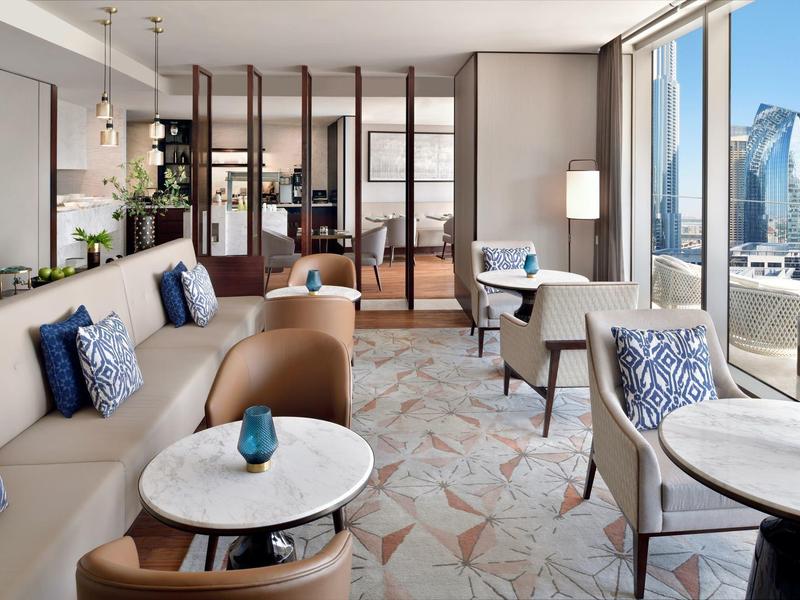 Moderner Wohnraum mit beigen Sofas, blauen Kissen, runden Tischen und großen Fenstern zur Stadtseite.