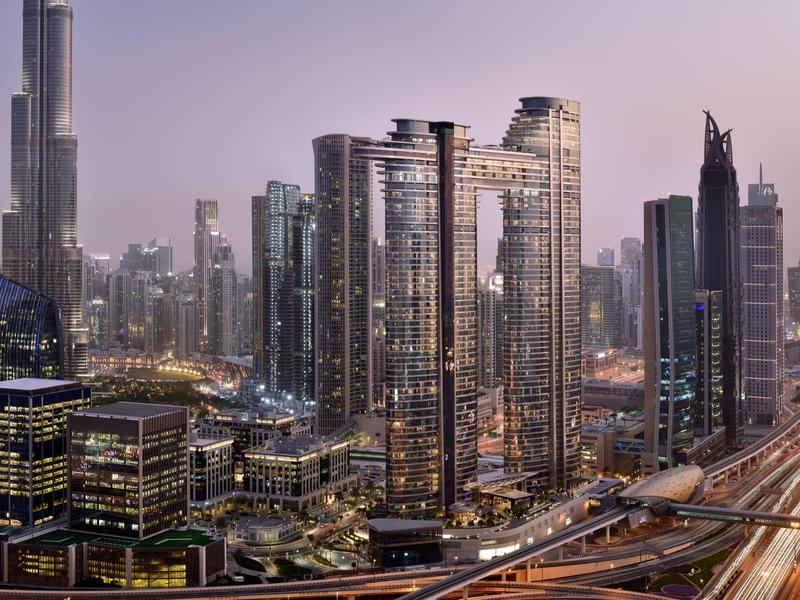 Moderne Wolkenkratzer und beleuchtete Straßen in einer Großstadt bei Dämmerung mit klarer Skyline.