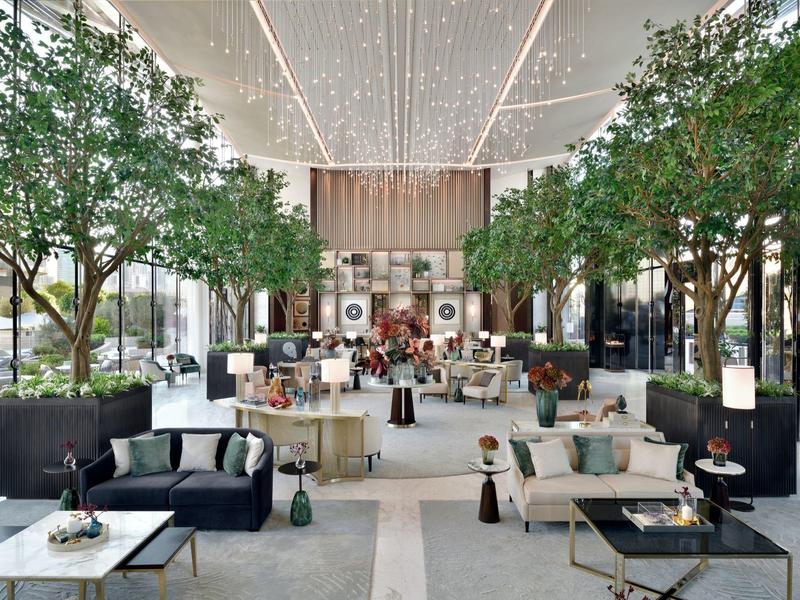 Großer, heller Innenraum mit modernen Sitzbereichen, vielen grünen Bäumen und beleuchtetem Deckendach.