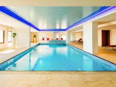 Hallenbad mit blauem Licht an der Decke und Sitzbereich im Hintergrund.