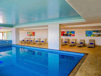 Klares bläulich leuchtendes Wasser im Pool neben Hotel mit Palmen und blauem Himmel.