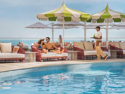 Luxuriöse Poollandschaft mit Liegestühlen und Sonnenschirmen am Meer, Gäste entspannen sich.