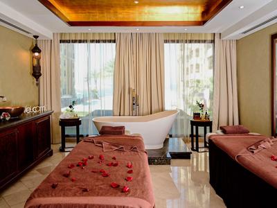 Eleganter Spa-Raum mit zwei Massageliegen, freistehender Wanne und warmem Holzdekor.