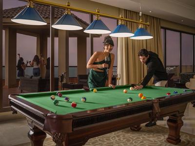 Zwei Personen spielen abends Billard in einem stilvoll eingerichteten Raum mit großen Fenstern.