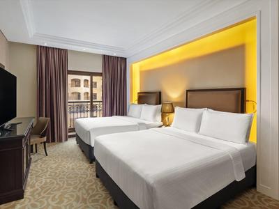 Hotelzimmer mit zwei Doppelbetten, Fernseher, Schreibtisch und Balkon mit Stadtblick.