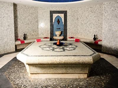 Ein luxuriöser Hamam-Raum mit einem zentralen großen Marmortisch und Sitzpolstern an den Wänden.