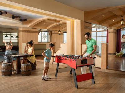 Zwei Kinder und zwei Erwachsene spielen Tischkicker und Tischtennis in einem hellen Freizeitraum.