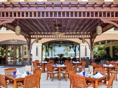 Außenrestaurant unter Holzpergola mit eingedeckten Tischen und Blick auf den Pool und Palmen.