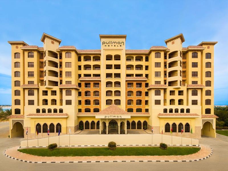 Großes, gelbes Hotel mit mehreren Etagen und symmetrischer Fassade unter blauem Himmel.