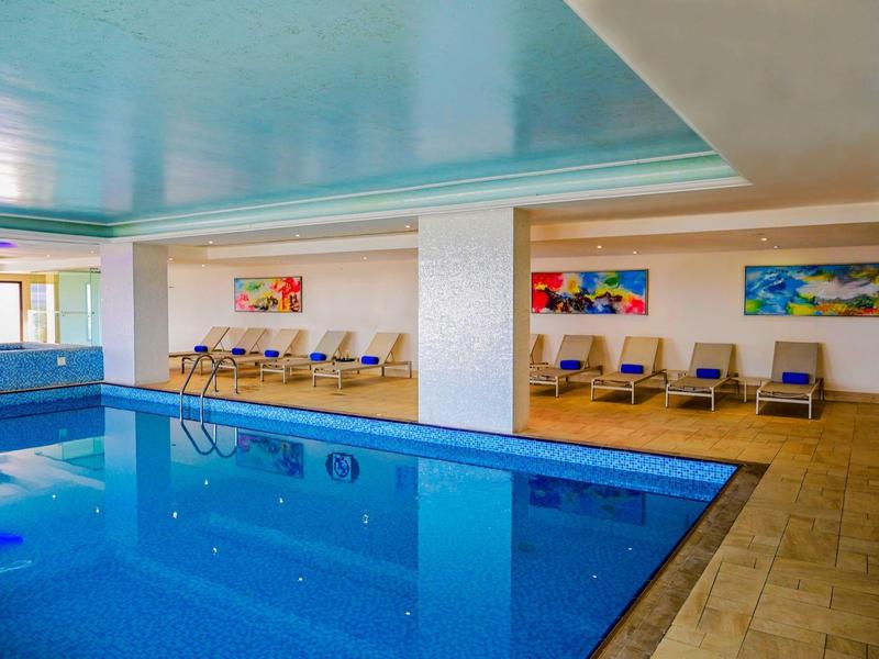 Klares bläulich leuchtendes Wasser im Pool neben Hotel mit Palmen und blauem Himmel.