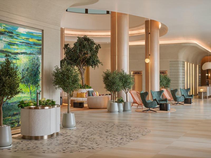 Heller Hotel-Lobbybereich mit Pflanzen, moderner Beleuchtung und Sitzgelegenheiten.