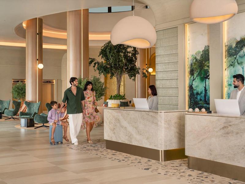 Moderner Hotel-Empfang mit zwei Rezeptionisten und einer Familie mit zwei Kindern.