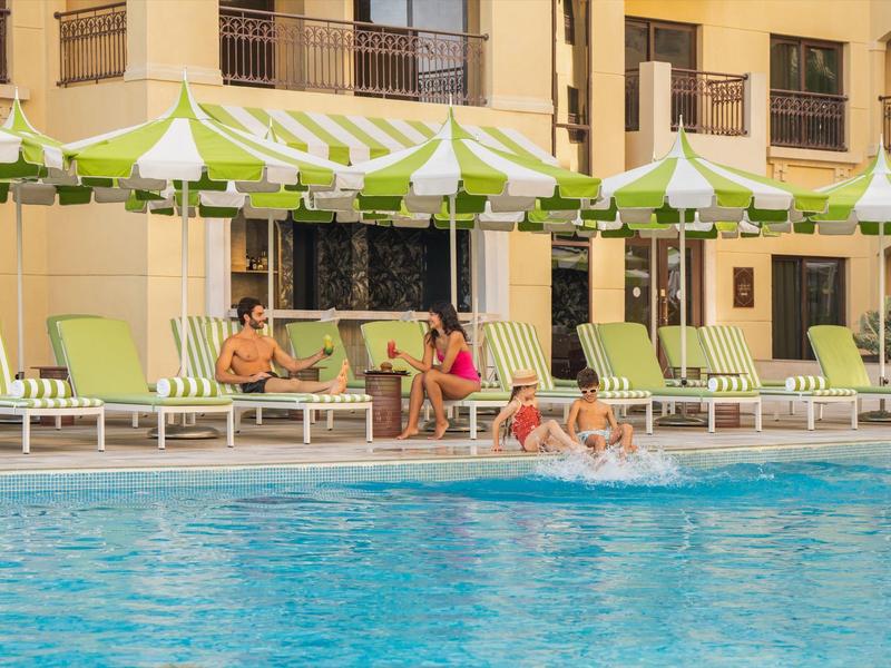 Hotelpool mit Gästen auf Liegestühlen und Kindern, die im Wasser spielen
