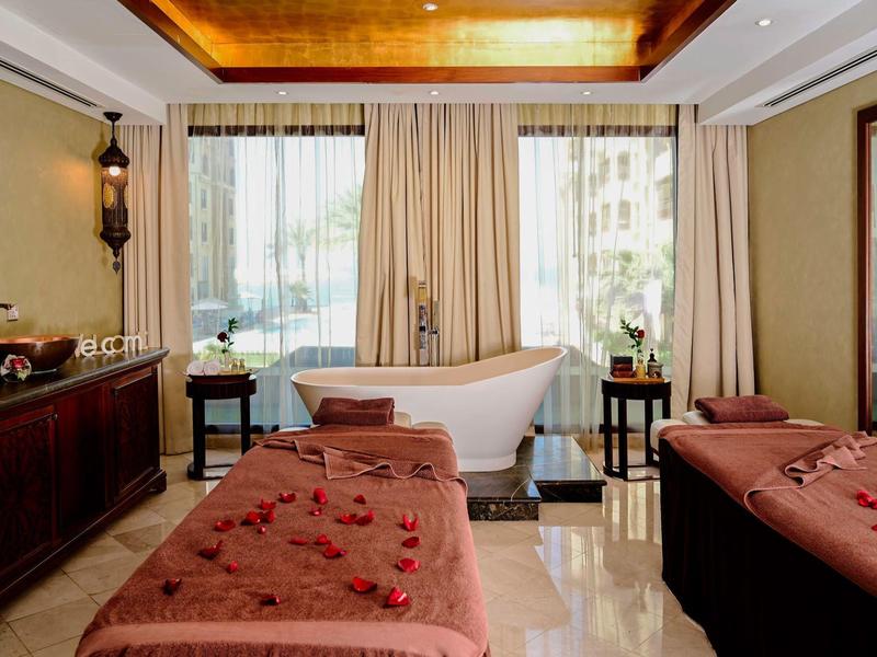 Eleganter Spa-Raum mit zwei Massageliegen, freistehender Wanne und warmem Holzdekor.