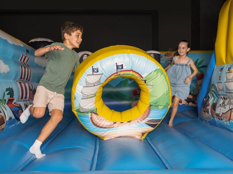 Kinder spielen auf einer aufblasbaren Hüpfburg mit maritimem Thema und großer Röhre