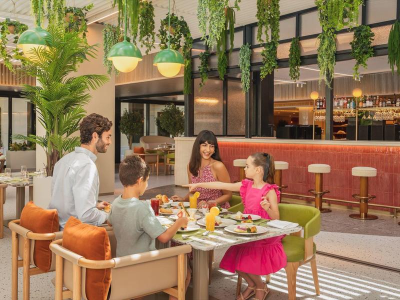 Familie isst zusammen in einem modernen Hotelrestaurant mit Pflanzen und Bartheke.