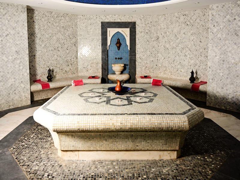 Ein luxuriöser Hamam-Raum mit einem zentralen großen Marmortisch und Sitzpolstern an den Wänden.