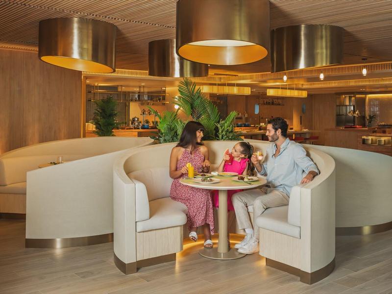 Drei Personen sitzen an einem runden Tisch in einer modernen Hotelbar mit bequemen Sitznischen.