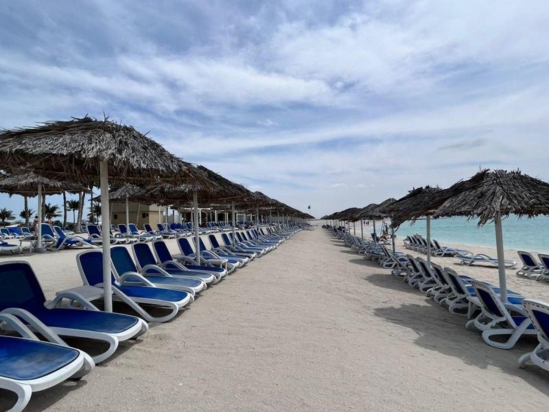 Sandstrand mit Reihen von leeren blauen Liegestühlen und Strohdächern unter bewölktem Himmel