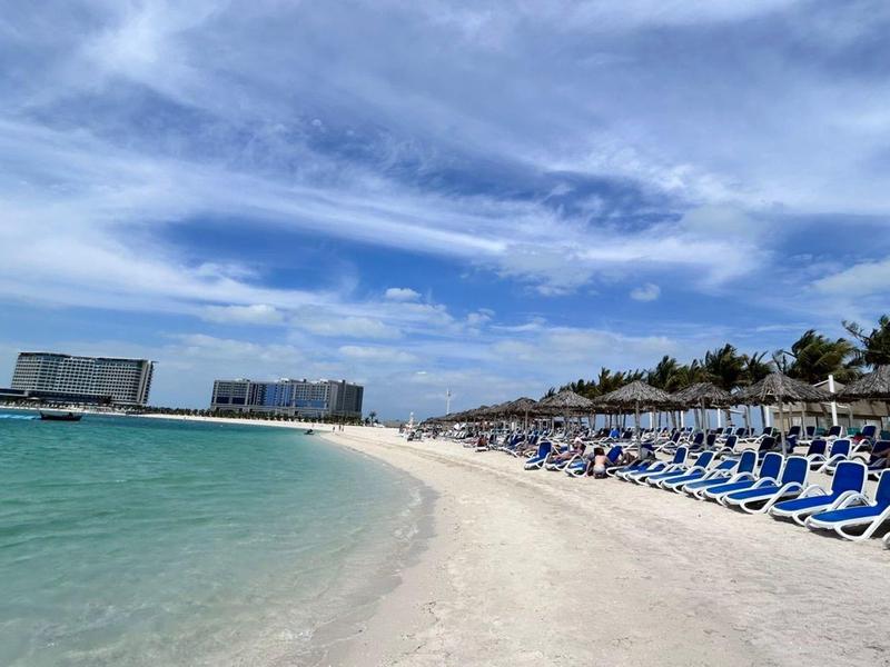 Strand mit Liegestühlen und türkisfarbenem Meer unter blauem Himmel mit Wolken