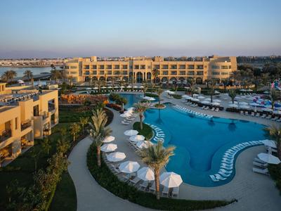 Hotelanlage mit großem Pool, Liegestühlen und Palmen bei Sonnenaufgang