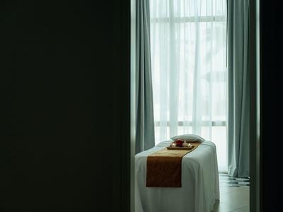 Salle de traitement avec table de massage et lumière naturelle à travers une fenêtre avec des rideaux.
