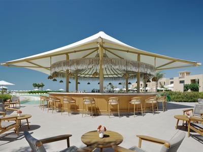 Modern outdoor bar area with stools and chairs under a large white sunshade.