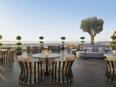 Modern outdoor terrace with round tables, chairs, and a large plant at sunset.
