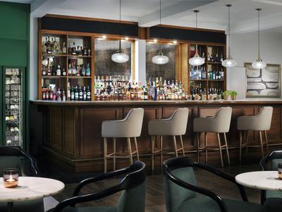 Modern hotel bar area with wooden counter, bar stools, and round tables with candles.