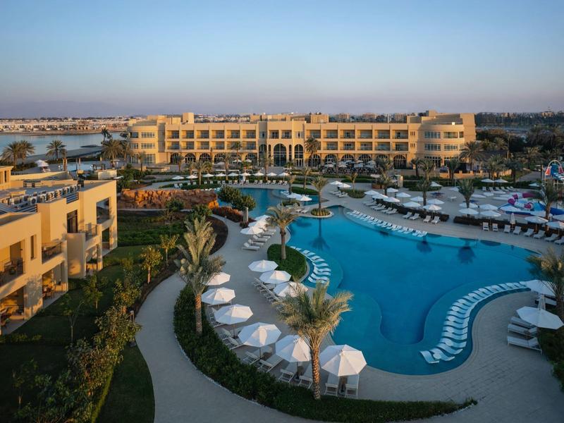 Complexe hôtelier avec grande piscine, transats et palmiers au lever du soleil