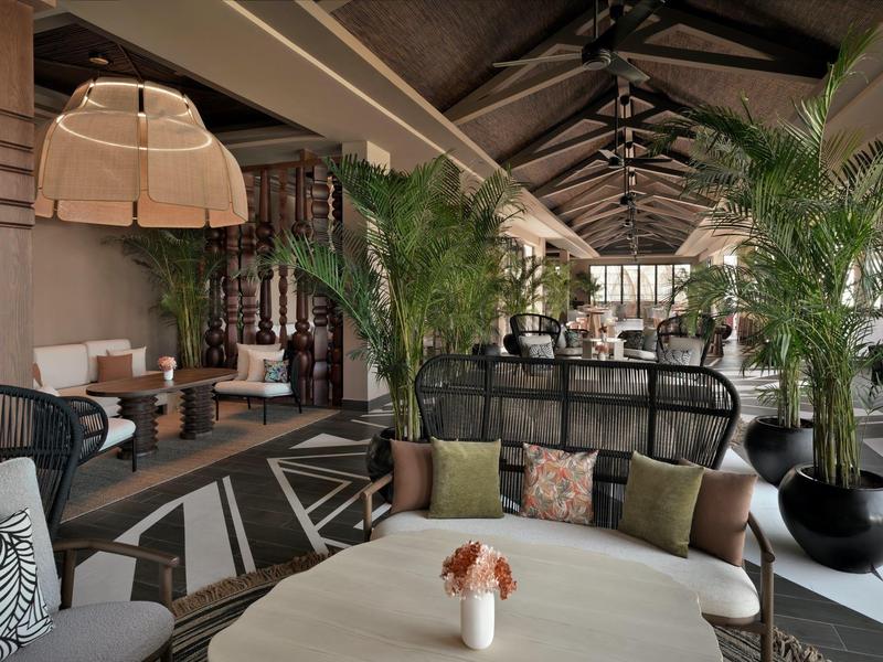 Salon moderne avec grandes plantes, sièges confortables et lampes élégantes.