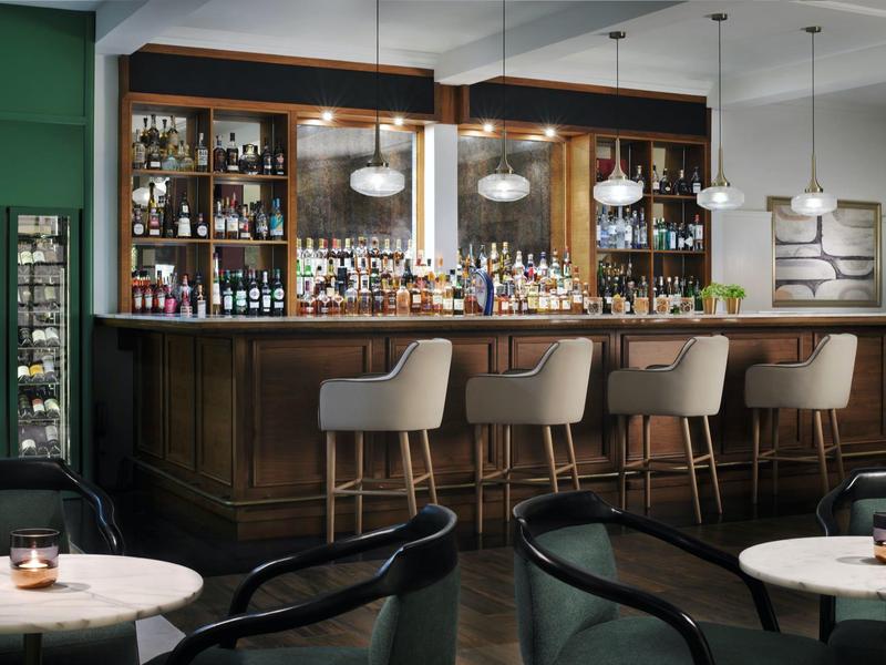 Bar d'hôtel élégante avec comptoir en bois haut et tabourets en cuir.