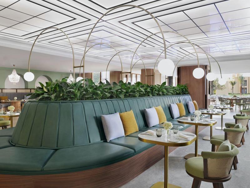 Restaurant d'hôtel moderne avec banquette verte courbée, tables rondes et élégantes lampes sphériques.