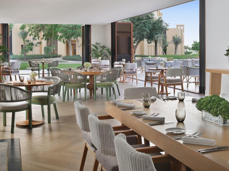 Restaurant moderne avec grandes fenêtres donnant sur une cour avec arbres et coin salon.