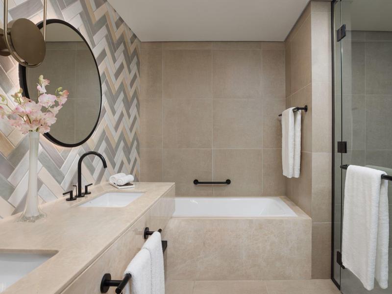 Salle de bain moderne avec baignoire, grande douche, miroir rond et carreaux muraux à motifs.
