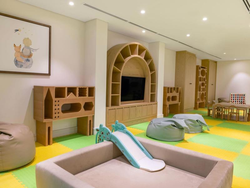 Salle de jeux pour enfants avec télévision, poufs confortables et sol coloré dans un hôtel.