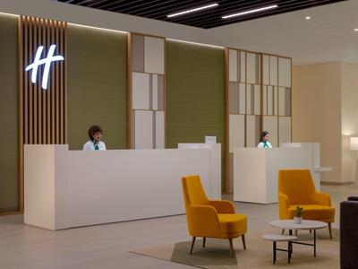 Moderner Empfangsbereich mit weißem Tresen, grünen Wandpaneelen und zwei gelben Sesseln.