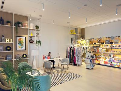 Innenraum eines modernen Ladens mit Regalen, Kleidung, Pflanzen und Sitzbereich mit Teppich.