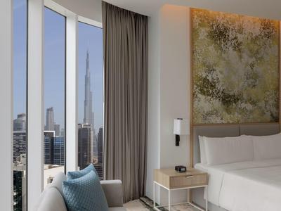 Modernes Schlafzimmer mit großem Fenster, grauer Couch, blauer Kissen und Stadtblick, helle Farben.