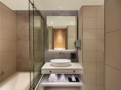 Modernes Badezimmer mit beige gekachelten Wänden, Glasdusche, rundem Aufsatzwaschbecken und großem Spiegel.