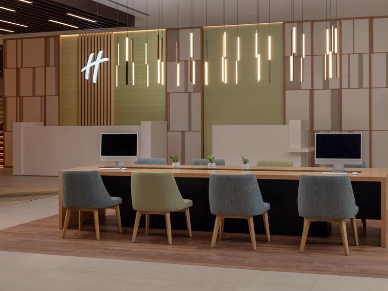 Moderner Konferenztisch mit bunten Stühlen und schwebenden Pendelleuchten in hellem Büroraum.