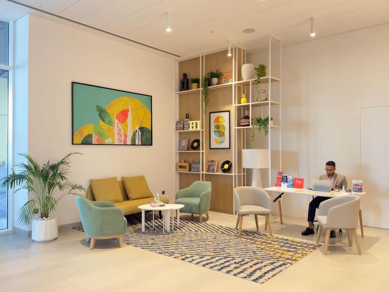 Moderner, heller Wohnraum mit gelbem Sofa, grünen Sesseln, Teppich und Bücherregal.