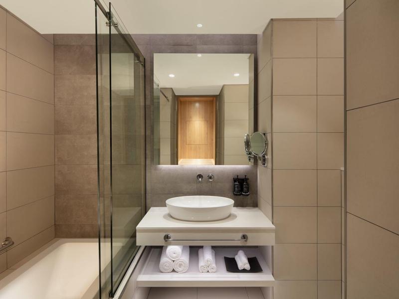 Modernes Badezimmer mit beige gekachelten Wänden, Glasdusche, rundem Aufsatzwaschbecken und großem Spiegel.